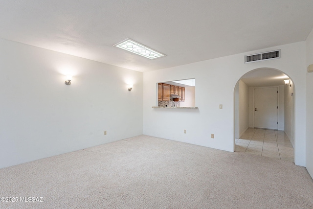 empty room featuring light colored carpet, visible vents, arched walkways, and light tile patterned floors