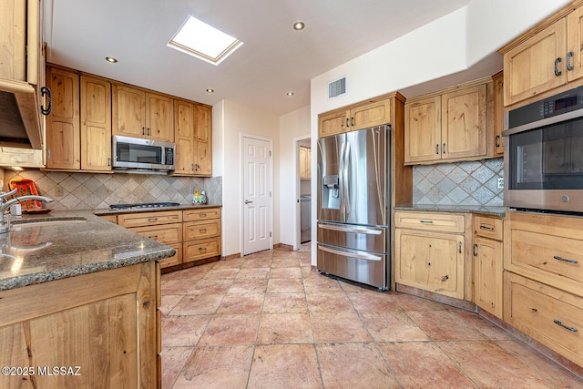 kitchen featuring backsplash, dark stone countertops, sink, and appliances with stainless steel finishes