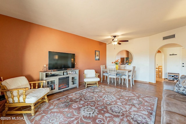 tiled living room with ceiling fan and a fireplace