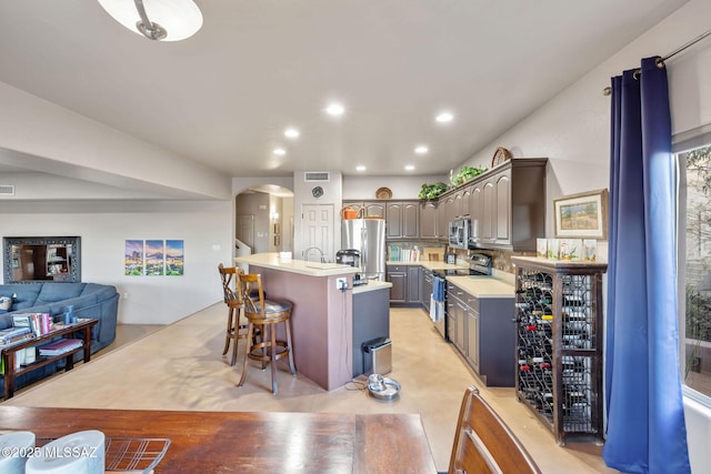 kitchen featuring a breakfast bar area, a center island with sink, arched walkways, stainless steel appliances, and light countertops