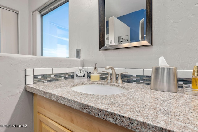 bathroom featuring vanity, a textured wall, and tasteful backsplash