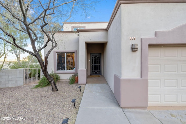 doorway to property featuring a gate, stucco siding, an attached garage, and fence