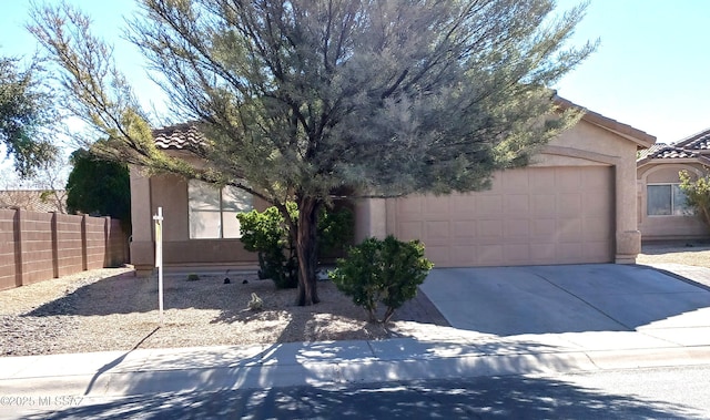 view of property hidden behind natural elements featuring an attached garage, fence, a tile roof, concrete driveway, and stucco siding