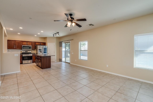 kitchen featuring ceiling fan, stainless steel appliances, light tile patterned floors, stone countertops, and a kitchen island