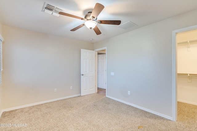 unfurnished bedroom with a closet, a spacious closet, ceiling fan, and light colored carpet