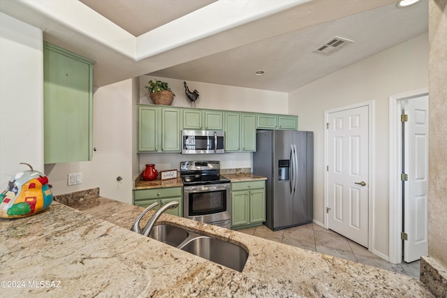 kitchen featuring green cabinets, sink, light stone countertops, light tile patterned flooring, and stainless steel appliances