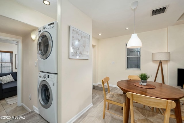 laundry area with light hardwood / wood-style floors and stacked washer and clothes dryer