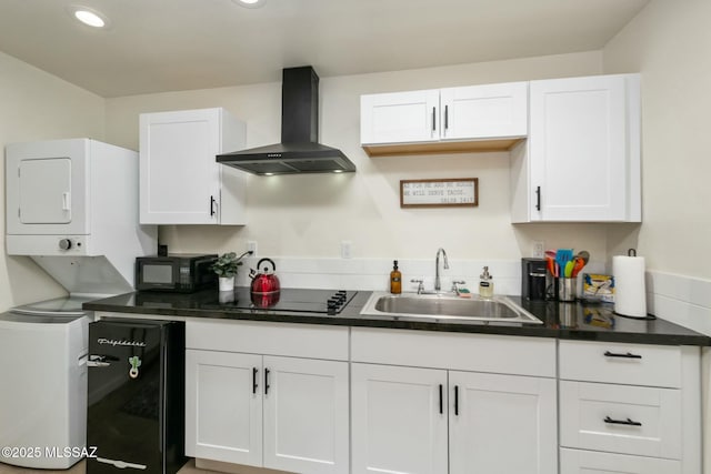 kitchen featuring stacked washer / dryer, sink, white cabinets, black appliances, and wall chimney exhaust hood