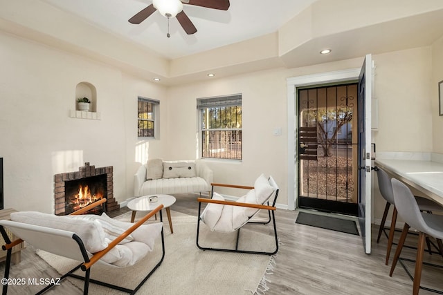 living room with a fireplace, ceiling fan, and light wood-type flooring