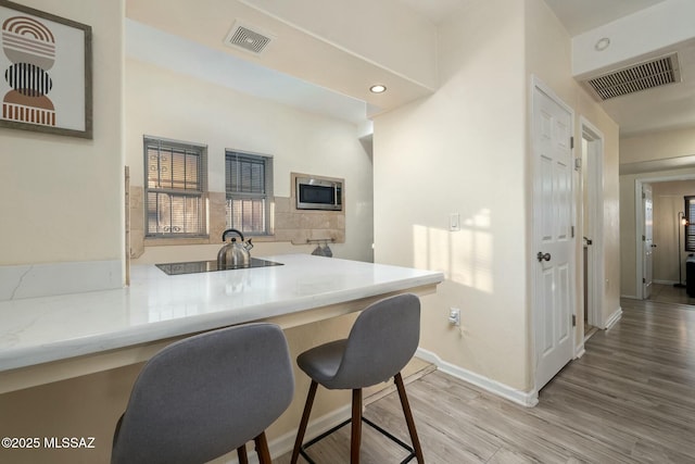 kitchen with hardwood / wood-style flooring, stainless steel microwave, a kitchen bar, and kitchen peninsula