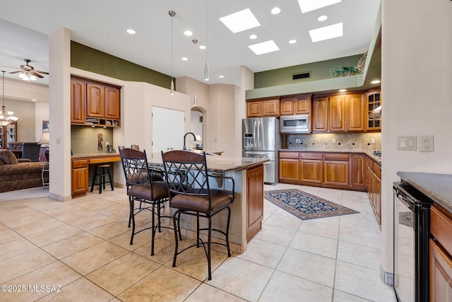 kitchen featuring light tile patterned floors, a breakfast bar, stainless steel appliances, a center island with sink, and beverage cooler