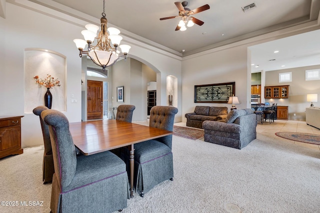 dining space featuring crown molding, a towering ceiling, ceiling fan with notable chandelier, and light carpet