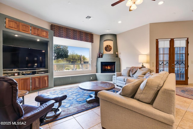 tiled living room featuring ceiling fan, a fireplace, and french doors