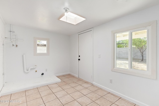 empty room with a skylight, plenty of natural light, baseboards, and light tile patterned floors