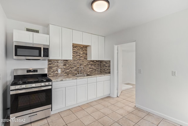 kitchen featuring a sink, white cabinetry, appliances with stainless steel finishes, light tile patterned flooring, and decorative backsplash