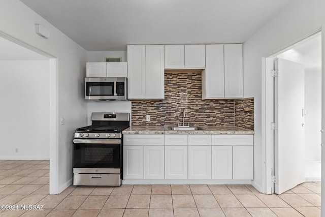 kitchen with light tile patterned flooring, backsplash, appliances with stainless steel finishes, and a sink