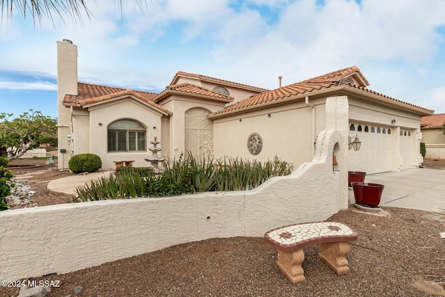 mediterranean / spanish-style house with a tile roof, concrete driveway, stucco siding, a chimney, and an attached garage