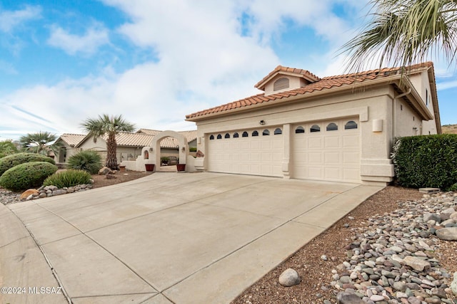 mediterranean / spanish-style house with concrete driveway, a tiled roof, an attached garage, and stucco siding