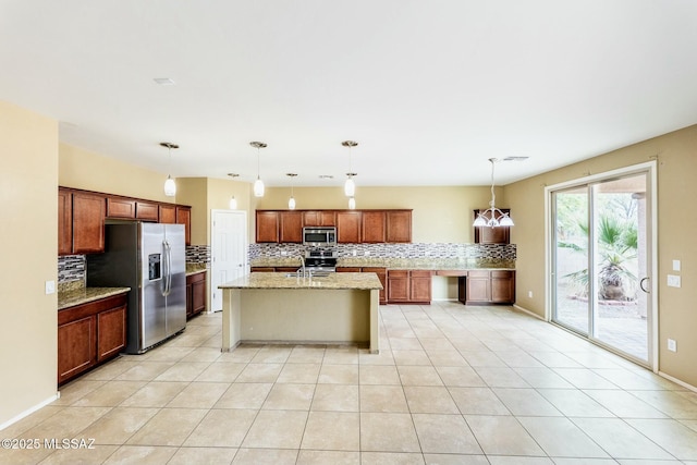 kitchen with light tile patterned flooring, hanging light fixtures, a kitchen island with sink, light stone counters, and stainless steel appliances