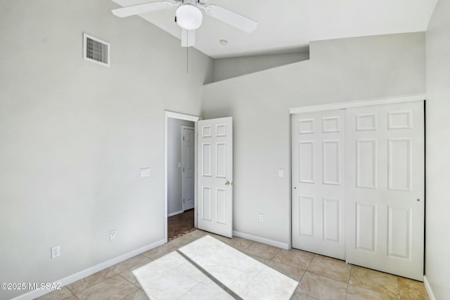 unfurnished bedroom with light tile patterned floors, high vaulted ceiling, a closet, and ceiling fan