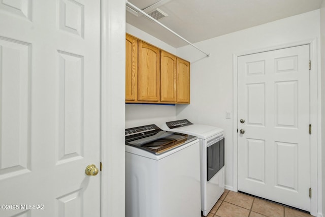 clothes washing area featuring cabinets, light tile patterned floors, and washing machine and clothes dryer