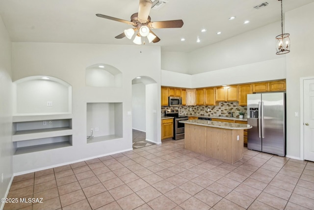 kitchen with light tile patterned flooring, appliances with stainless steel finishes, a kitchen island, a high ceiling, and built in shelves