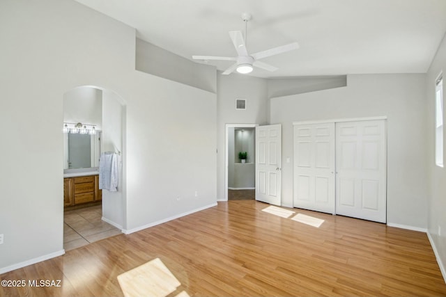 unfurnished bedroom with ensuite bathroom, high vaulted ceiling, a closet, ceiling fan, and light hardwood / wood-style flooring