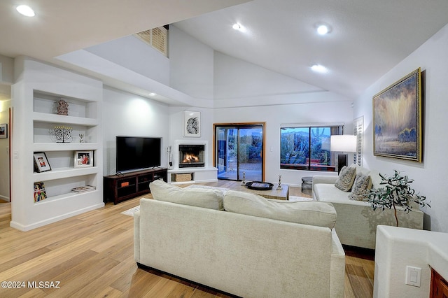 living room with built in shelves, a high ceiling, and light hardwood / wood-style flooring