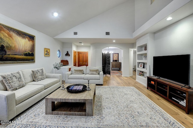 living room with a notable chandelier, built in shelves, wood-type flooring, and high vaulted ceiling