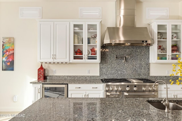 kitchen featuring white cabinetry, dark stone countertops, beverage cooler, wall chimney range hood, and high end stainless steel range