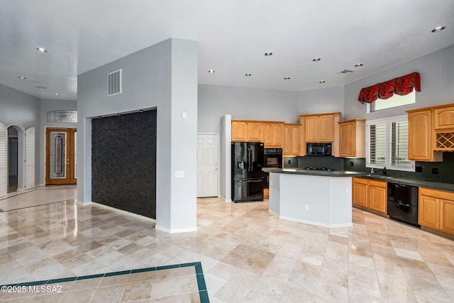 kitchen featuring a center island, sink, a towering ceiling, decorative backsplash, and black appliances