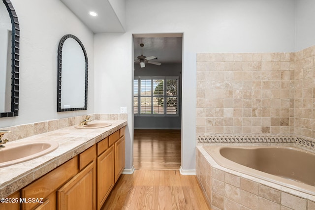 bathroom featuring hardwood / wood-style flooring, ceiling fan, a relaxing tiled tub, and vanity