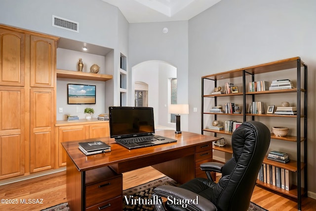 office space featuring a high ceiling, light hardwood / wood-style floors, and built in features