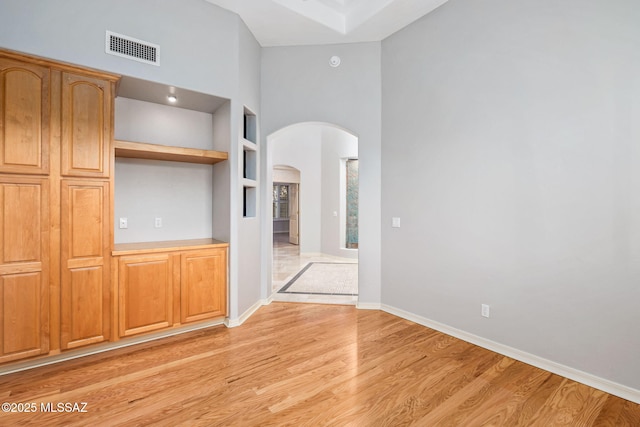 unfurnished living room featuring built in features, a towering ceiling, and light hardwood / wood-style flooring