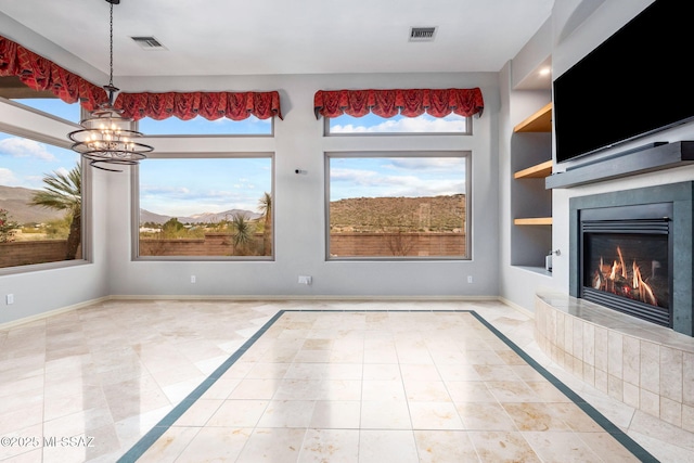 unfurnished dining area featuring a fireplace, built in shelves, tile patterned flooring, and an inviting chandelier