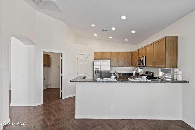 kitchen featuring lofted ceiling, appliances with stainless steel finishes, dark parquet floors, kitchen peninsula, and dark stone counters