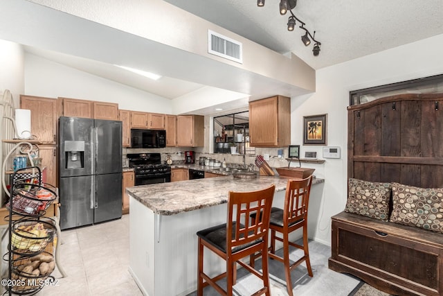 kitchen featuring kitchen peninsula, vaulted ceiling, black appliances, and tasteful backsplash