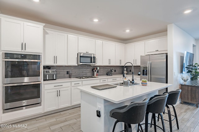 kitchen with appliances with stainless steel finishes, sink, a kitchen island with sink, and white cabinets