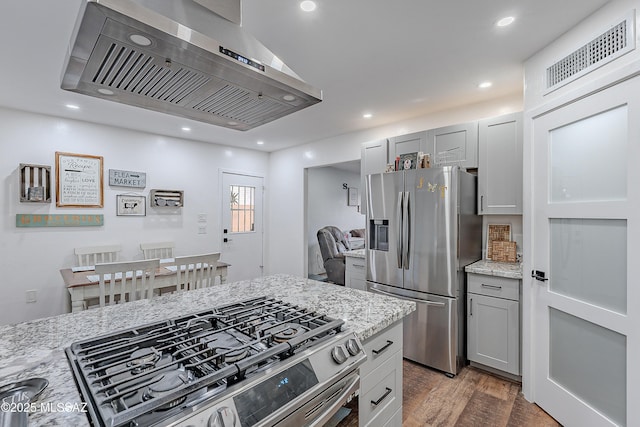 kitchen featuring gray cabinetry, light stone counters, stainless steel appliances, and wall chimney range hood