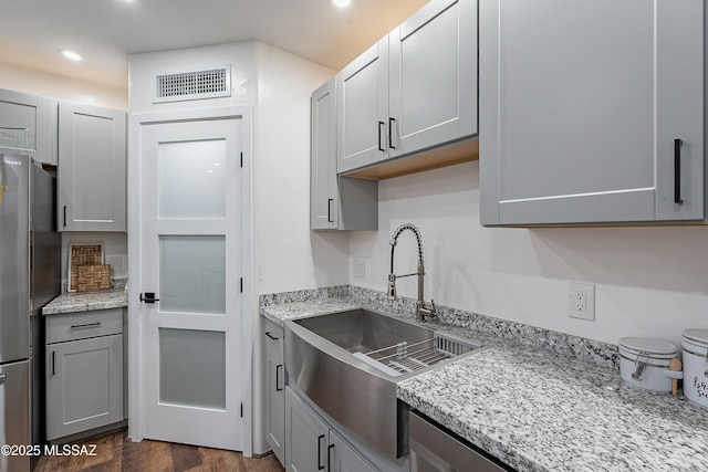 kitchen with stainless steel fridge, light stone counters, gray cabinetry, sink, and dark hardwood / wood-style floors