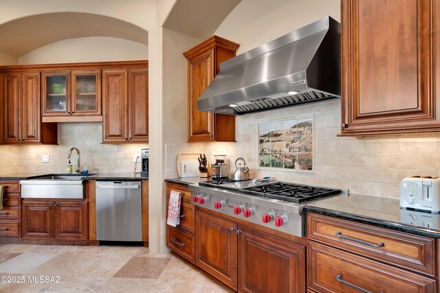 kitchen featuring appliances with stainless steel finishes, wall chimney exhaust hood, tasteful backsplash, and dark stone counters