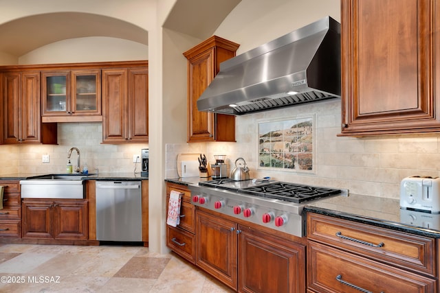 kitchen with dark stone countertops, decorative backsplash, stainless steel appliances, and wall chimney exhaust hood