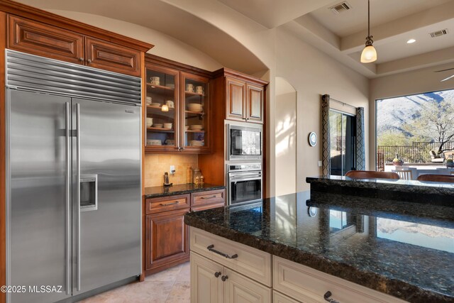 kitchen featuring tasteful backsplash, dark stone countertops, built in appliances, and pendant lighting