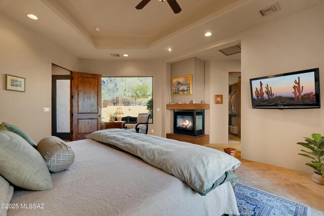 tiled bedroom featuring ceiling fan, a multi sided fireplace, and a tray ceiling