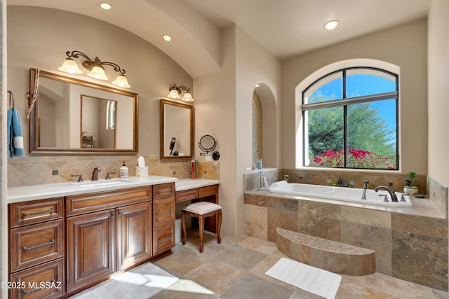 bathroom with vanity, a relaxing tiled tub, and decorative backsplash