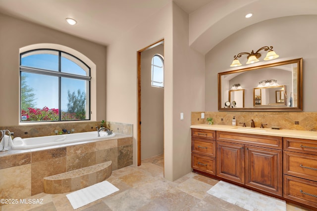 bathroom with decorative backsplash, tiled tub, and vanity