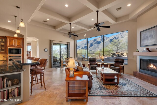 living room featuring ceiling fan, beamed ceiling, a high ceiling, a mountain view, and coffered ceiling