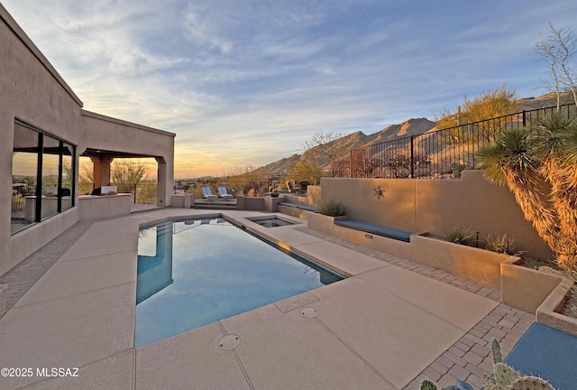 pool at dusk featuring a hot tub, exterior kitchen, and a patio area