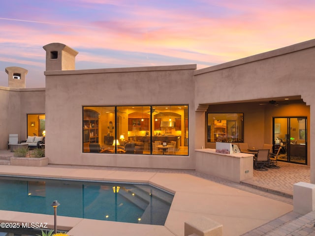 pool at dusk with ceiling fan and a patio area