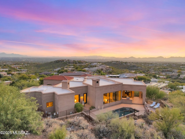 back house at dusk featuring a mountain view and a patio area